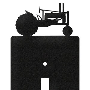 May include: Black metal light switch cover featuring a tractor silhouette at the top. The cover has a rectangular shape with a toggle switch opening and two screw holes. A decorative farm-themed accent.