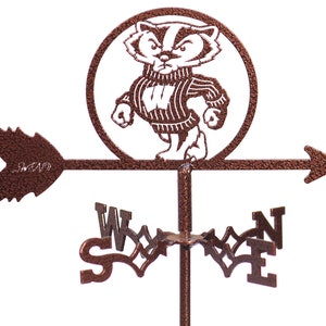May include: A brown metal weather vane featuring a stylized badger wearing a sweater with the letter "W" on it. The badger is in a circle with a white background. The weather vane also has a directional arrow and the letters N, S, E, and W.