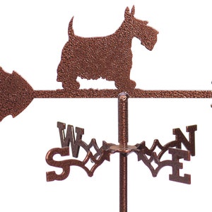 May include: A copper-coloured metal weather vane featuring a silhouette of a Scottish Terrier dog. The vane has a directional arrow and compass points labelled with the letters N, S, E, and W.