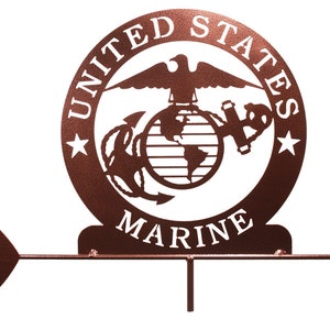 K&ouml;nnte beinhalten: Ein brauner Windfahne aus Metall mit einem wei&szlig;en Pfeil und einem kreisf&ouml;rmigen Design mit dem Emblem des United States Marine Corps. Das Emblem enth&auml;lt einen Globus, einen Adler und einen Anker. Die Worte "United States Marine" sind auf die Windfahne eingraviert.