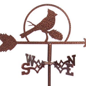 May include: A copper-colored metal cardinal weather vane with a compass rose and an arrow pointing to the east. The cardinal is perched on a branch with a sun behind it.