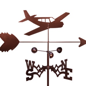 May include: A brown metal airplane weather vane with a compass rose and four cardinal directions. The compass rose is made of metal and has a decorative design. The weather vane is mounted on a metal pole.