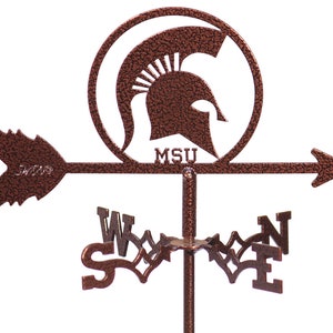 May include: A copper-colored metal weather vane featuring a Spartan helmet with the letters "MSU" below it. The vane has an arrow pointing to the east and a compass rose with the letters N, S, E, and W.