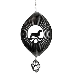 May include: Black metal wind chime featuring a dachshund silhouette and a paw print charm. The chime is made of multiple concentric circles that spin in the wind.