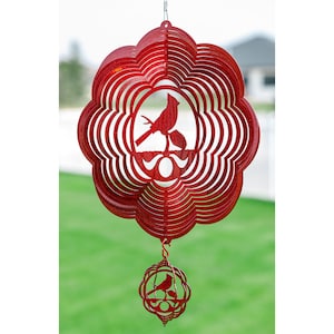 May include: Red metal wind spinner with a cardinal silhouette. The spinner has multiple layers and a smaller ball with a cardinal silhouette hanging below.