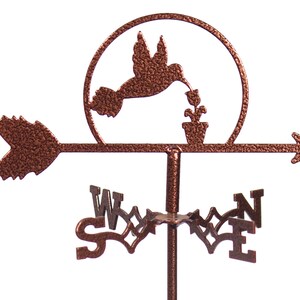 May include: A copper-colored metal hummingbird wind spinner with a flower and a pot. The wind spinner has a circular base with a hummingbird silhouette and a flower in a pot. The wind spinner has an arrow-shaped pointer with a copper-colored finish.