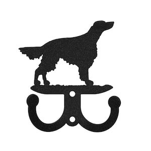 May include: Black metal wall hook featuring a silhouette of a dog. The hook has two curved arms and a decorative dog figure above. The dog is standing on a curved platform. The hook is designed for hanging items.