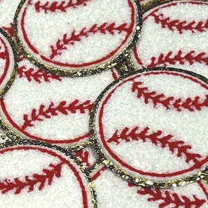 Könnte beinhalten: Nahaufnahme von Baseball-Patches. Jedes Patch hat einen weißen Hintergrund mit roten Nähten und einem roten Rand. Die Patches sind mit goldenem Glitzer verziert.