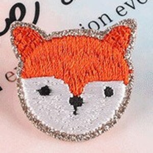 May include: Embroidered fox patch with orange fur, white face, and black eyes and nose. The patch is outlined with silver glitter. This decorative patch can be sewn or ironed onto clothing or accessories.