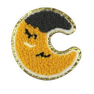 May include: Embroidered patch in the shape of a crescent moon. The moon features a textured yellow surface with a dark gray upper section and a white border. Two small black bats are flying across the moon, and the patch is outlined with gold glitter.