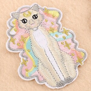 May include: Embroidered patch of a cat with a unicorn design. The patch has a white border and a light beige body. The cat's mane and wings are pastel colours with gold star accents. The cat has black eyes and a white chest.