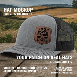May include: A gray and black trucker hat with a brown leather patch that says "YOUR PATCH DESIGN OF ANY SHAPE". The hat is sitting on a wooden surface with a blurred background of a field.