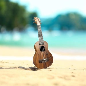 Op de afbeelding: Een bruine ukulele staat op een zandstrand met een vage oceaanachtergrond. Het instrument heeft een rond klankgat en vier snaren. De ukulele is gemaakt van hout en heeft een natuurlijke afwerking. Het strand is lichtbruin en het water is turquoise.