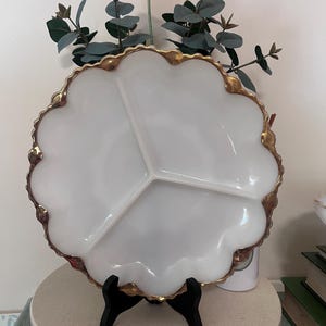 May include: White divided serving dish with a gold rim and scalloped edge. The dish is on a black stand.