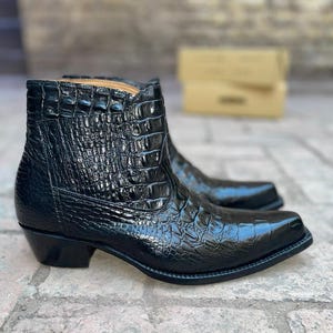 May include: A pair of black ankle boots featuring a glossy, textured crocodile skin pattern. These boots have a pointed toe, a stacked heel, and a high-cut shaft that reaches above the ankle, showcasing a polished finish and detailed scale texture.