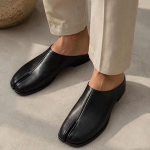 Peut inclure: Une paire de chaussures à enfiler en cuir noir avec un design à bout fendu distinctif. La chaussure présente une finition lisse, un petit talon et une couture centrale allant du bout fendu à l'ouverture, offrant un aspect élégant et fonctionnel.