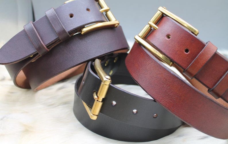 Pode incluir: Tr&ecirc;s cintos de couro nas cores castanho escuro, castanho m&eacute;dio e preto, cada um com um acabamento liso e uma fivela de metal dourado polido. Os cintos est&atilde;o dispostos em grupo, exibindo os v&aacute;rios tons de couro e as ferragens met&aacute;licas.
