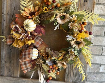 May include: A fall-themed wreath with sunflowers, pumpkins, berries, and autumn leaves. The wreath is adorned with a plaid ribbon and is hanging on a rustic wooden door. A metal sign that says "HOME" is at the top.