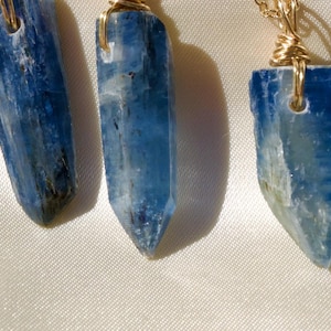 May include: Five gold necklaces with blue crystal pendants. Each pendant is a long, thin, pointed crystal with a wire wrap.