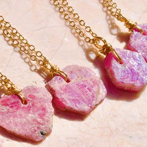 May include: Three gold chain necklaces with pink ruby crystal pendants. Each pendant is a different shape and size, and they are all attached to the chains with gold wire.