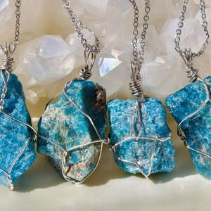 May include: Four turquoise blue gemstone pendants wrapped in silver wire, hanging from silver chains. The gemstones are rough and have a natural, organic look.
