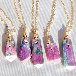 May include: Five gold chain necklaces with pink and green gemstone pendants. Each pendant is wrapped in gold wire and has a unique pattern.