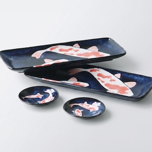 May include: Two rectangular ceramic plates and two small round ceramic dishes, all featuring a deep navy blue glaze with hand-painted white and orange koi fish motifs. The plates are elongated with slightly raised edges, while the dishes are circular.
