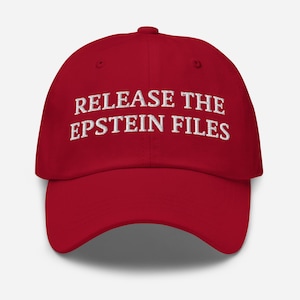 Może przedstawiać: Czerwona czapka bejsbolowa z białym haftem "RELEASE THE EPSTEIN FILES". Czapka ma zakrzywiony daszek i zapięcie na pasek z tyłu. Ten kapelusz to oświadczenie polityczne.