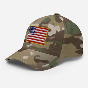 Peut inclure: Une casquette de baseball avec un motif camouflage dans des tons de vert, marron et beige. Le panneau avant présente un écusson rectangulaire brodé du drapeau des États-Unis avec des rayures rouges, blanches et bleues et un champ bleu étoilé.