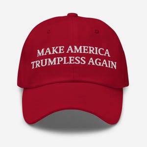 Op de afbeelding: Rode baseballcap met witte geborduurde tekst "MAKE AMERICA TRUMPLESS AGAIN". De cap heeft een gebogen klep en een verstelbare bandsluiting aan de achterkant.