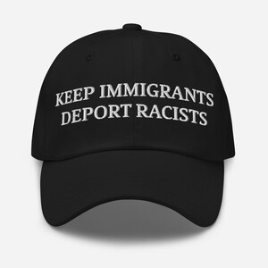 May include: Black baseball cap with white embroidered text that reads "KEEP IMMIGRANTS DEPORT RACISTS". The cap has a curved brim and an adjustable strap at the back. A simple, yet bold statement.