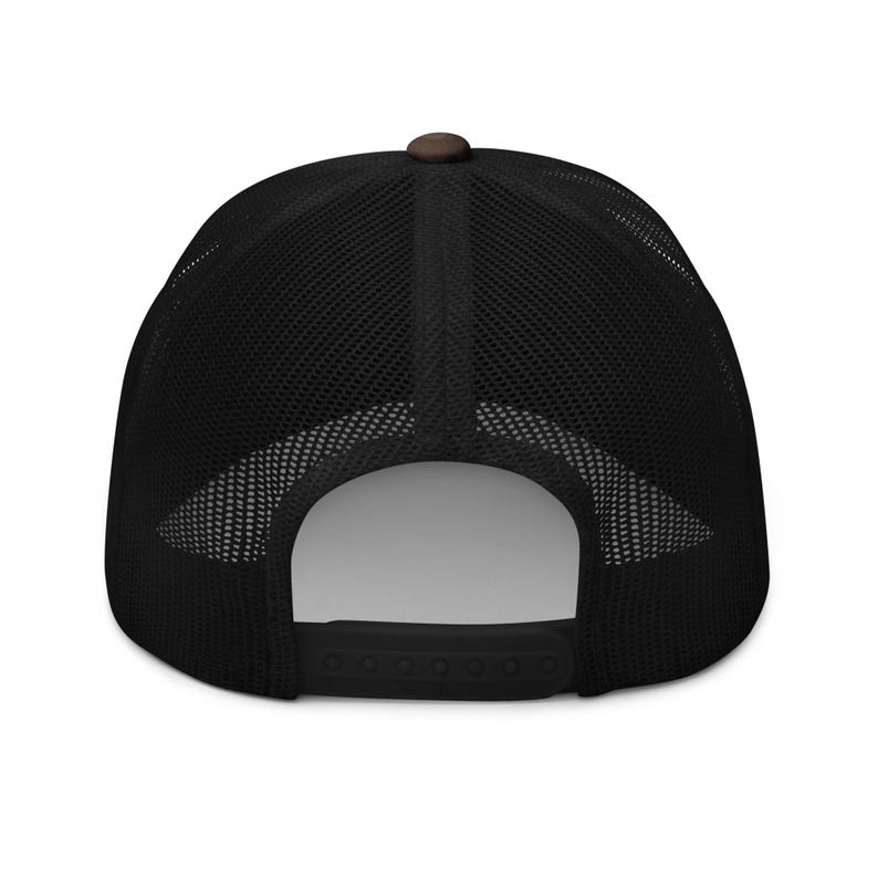 May include: Black trucker hat with a brown top button and a black mesh back. The hat has a curved brim and an adjustable snap closure at the back. The hat is a classic style.
