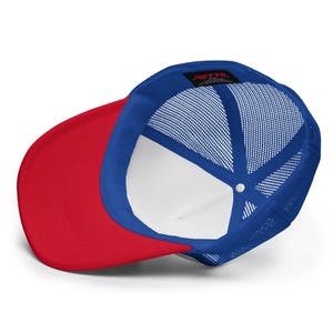May include: A trucker hat featuring a vibrant red brim and a bright blue mesh back panel. The interior of the cap displays a white front panel lining and a black tag with the red text OTTO printed on the inside crown of the headwear piece.