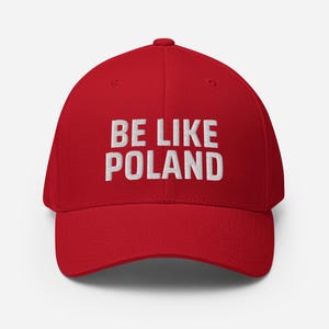 May include: A red baseball cap with the phrase "BE LIKE POLAND" embroidered in white block letters. The cap has a curved brim and a structured fit. The hat is a solid, vibrant red color.