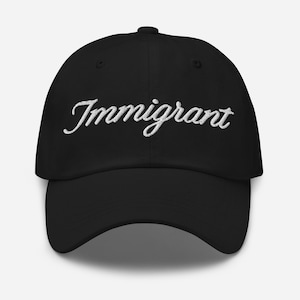 Puede incluir: Gorra de béisbol negra con la palabra "Immigrant" bordada en blanco en la parte delantera. La gorra tiene una visera curva y un botón en la parte superior. Un accesorio casual.