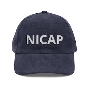 May include: Navy blue corduroy baseball cap with the word "NICAP" embroidered in white block letters across the front. The cap has a curved brim and a rounded top.