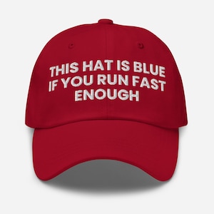 May include: A red baseball cap featuring white embroidered text on the front that reads: THIS HAT IS BLUE IF YOU RUN FAST ENOUGH. The cap has a structured crown, a curved brim, and a button at the top, showcasing a bold colour contrast throughout.