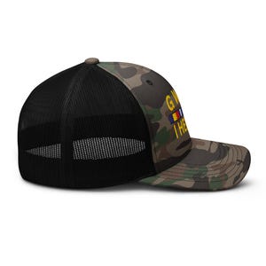 May include: Camouflage trucker hat with a black mesh back and a curved brim. The hat features the text "GW" above a small flag design and the text "I HEAR".