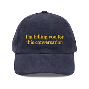 Op de afbeelding: Marineblauwe corduroy baseballcap met de gele geborduurde tekst "I'm billing you for this conversation". De cap heeft een gebogen klep en een knoop aan de bovenkant.
