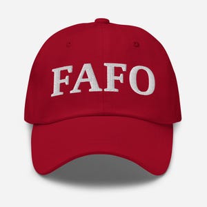 May include: A red baseball cap with the white embroidered letters "FAFO" across the front. The cap has a curved brim and a fabric strap closure on the back.