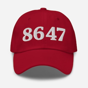 May include: A red baseball cap with the white embroidered number "8647" across the front. The cap has a curved brim and a rounded crown. The hat is made of a soft fabric.