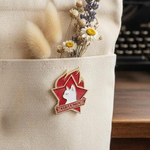 May include: A red and white enamel pin featuring a white cat silhouette inside a red star, with the text "ВСЕГДА КОТОВЫ" in red. The pin is attached to a beige canvas tote bag, with dried flowers in the pocket.