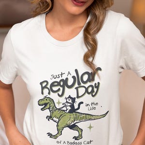Funny Cat T-Rex Unisex Tee, Cat Riding Dino Shirt, Retro Pet Lover Gift, Badass Cat Owner Tee, Vintage Aesthetic Top, Funny Animal Graphic
