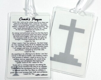 May include: Two clear plastic luggage tags with white inserts. One tag features the black printed text Coach's Prayer, while the other displays a gray cross graphic resting on a stepped base. Both tags include clear plastic loops for attachment.