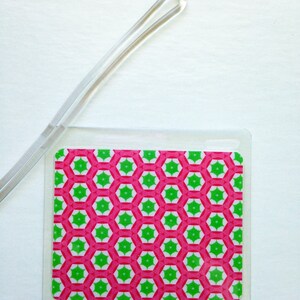 May include: A clear plastic ID badge holder with a pink and green geometric pattern. The pattern features a repeating hexagon design with white accents. A clear plastic lanyard is attached to the holder.