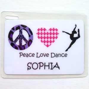 May include: A white plastic ID badge with a peace sign, heart, and dancer silhouette. The peace sign has a purple and black leopard print pattern. The heart is pink and white checkered. Text reads "Peace Love Dance" and "SOPHIA".