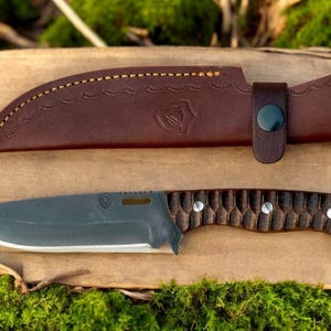 Puede incluir: Una funda de cuero marr&oacute;n con un bot&oacute;n negro y un cuchillo gris oscuro con mango de madera marr&oacute;n.