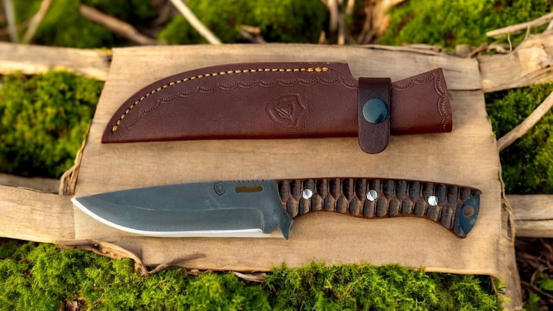 Puede incluir: Una funda de cuero marr&oacute;n con un bot&oacute;n negro y un cuchillo gris oscuro con mango de madera marr&oacute;n.