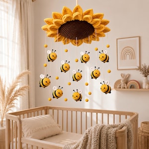 Könnte beinhalten: Ein hängendes Mobile mit einer großen, gehäkelten Sonnenblume mit dunkelbrauner Mitte und gelben Blütenblättern. Von der Blume hängen mehrere Schnüre mit kleinen, gehäkelten Hummeln mit schwarz-gelben Streifen und weißen Flügeln, durchsetzt mit kleinen gelben Garnkugeln.