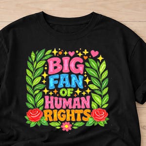 May include: Black t-shirt with the text "BIG FAN OF HUMAN RIGHTS" in colorful bubble letters. The text is surrounded by a wreath of green leaves, red roses, and stars.